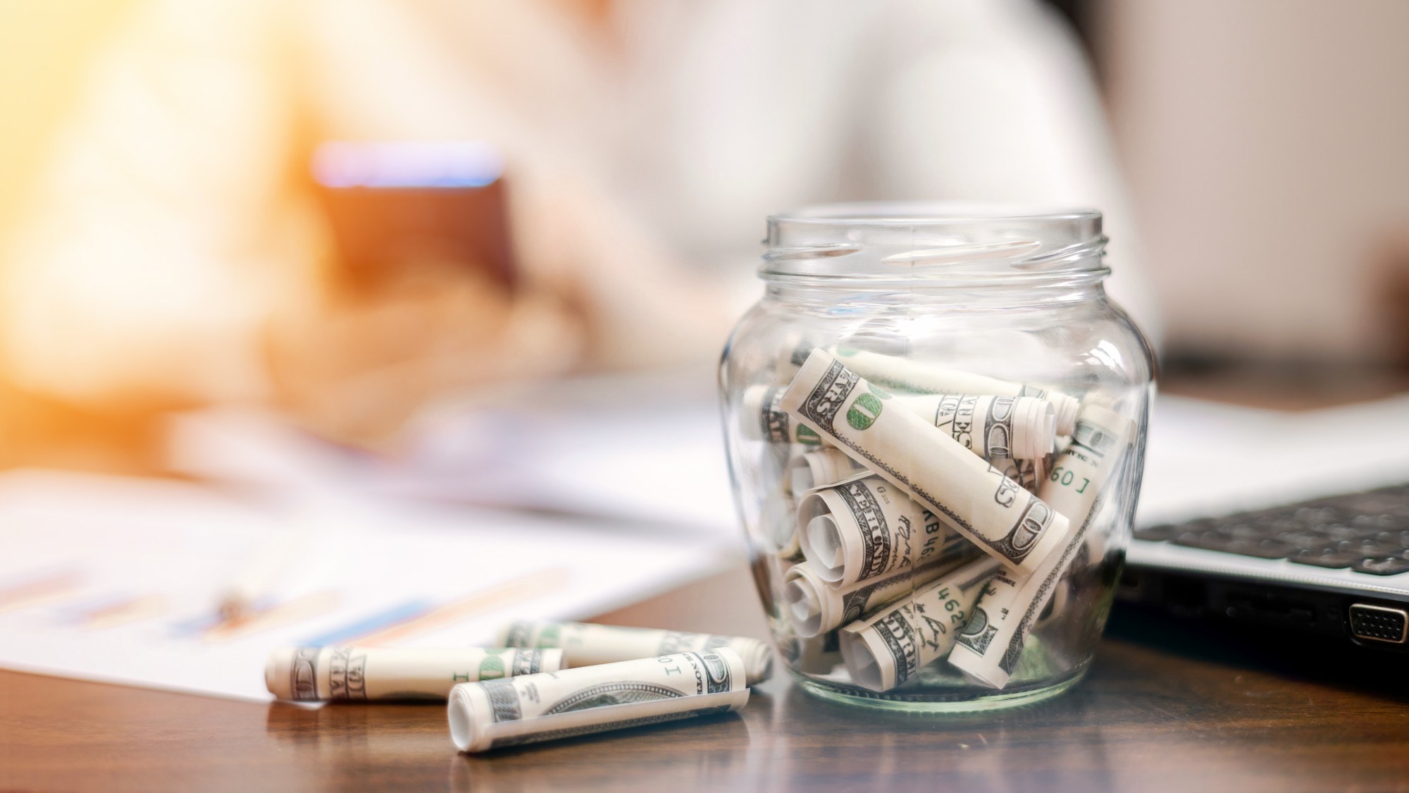[fpdl.in]_jar-with-rolled-banknotes-table-laptop-papers-woman-background_1268-17480_full